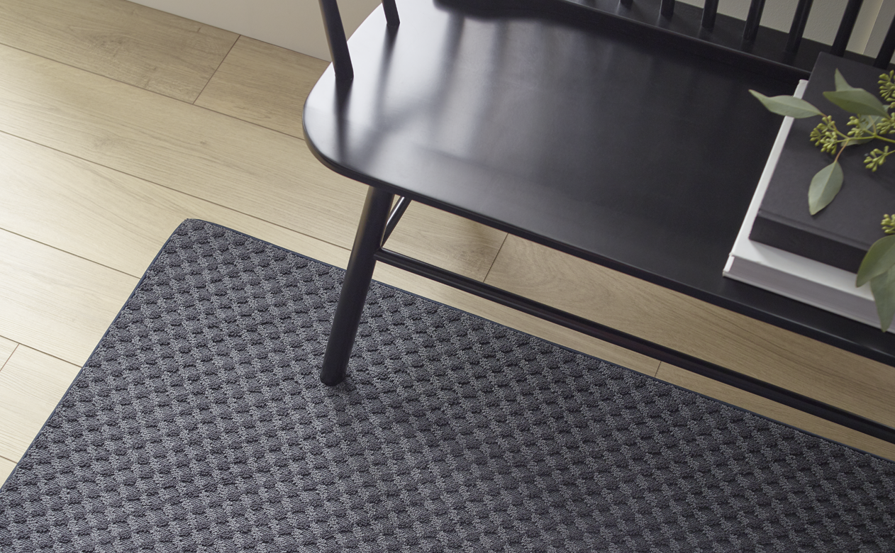 black patterned area rug in hall with light wood floors and black bench